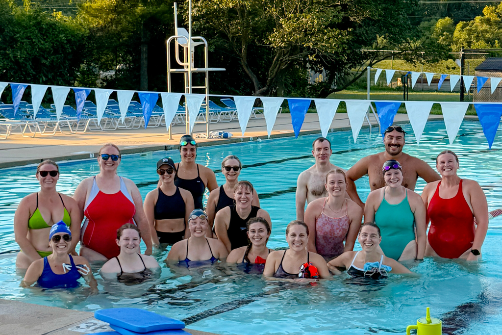 17 swimmers group together and smile at an outdoor pool. 